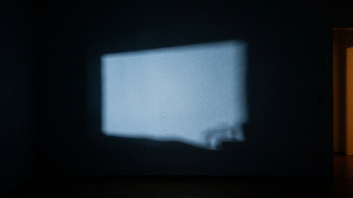 Das kalte Licht eines nicht sichtbaren Bildschirms liegt als unruhiges Rechteck auf einer dunklen Wand