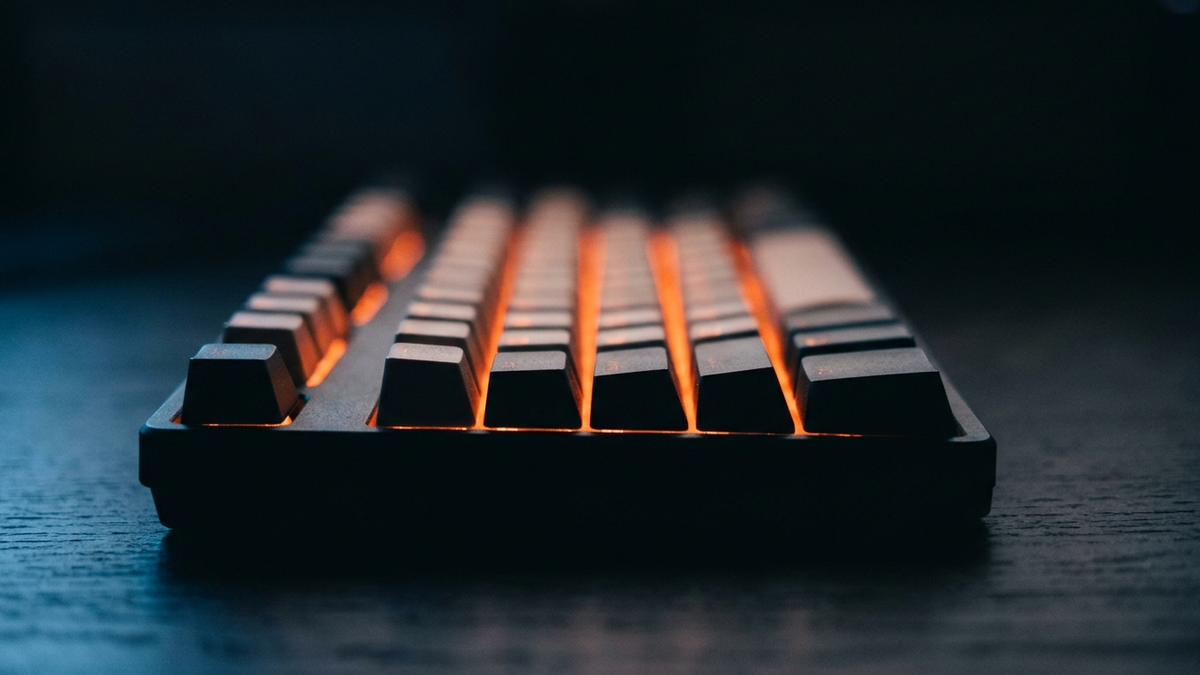 Eine mechanische Tastatur von der Seite auf Tischhöhe, zwischen den Tastenkappen glimmt orange Beleuchtung hervor
